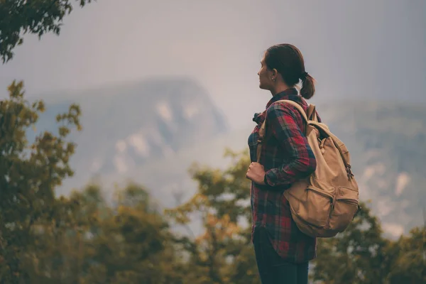 Hipster menina com mochila desfrutando do pôr do sol no pico da montanha nebulosa . — Fotografia de Stock