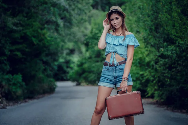 Pretty young woman hitchhiking along a road.