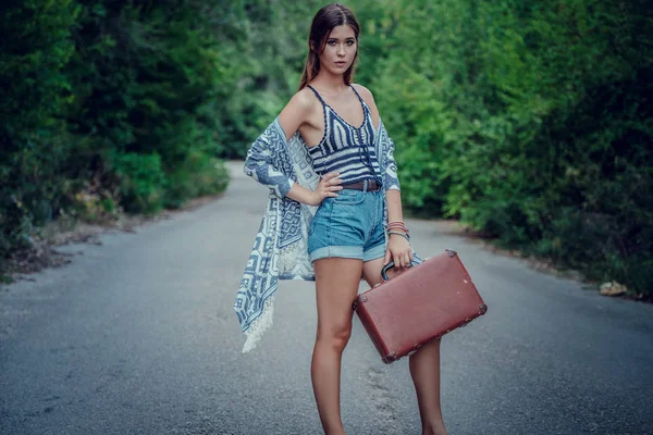 Pretty young woman hitchhiking along a road.