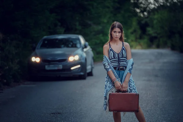 Pretty young woman hitchhiking along a road.