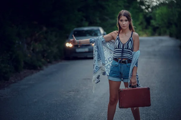Pretty young woman hitchhiking along a road.