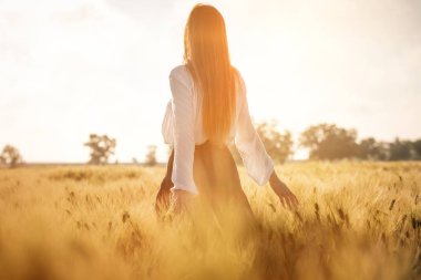 Gün batımında buğday alanında Kızıl saçlı kız.