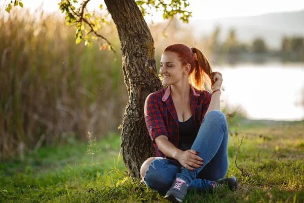 Atractiva joven disfrutando de su tiempo al aire libre en el parque con puesta de sol en el fondo. —  Fotos de Stock