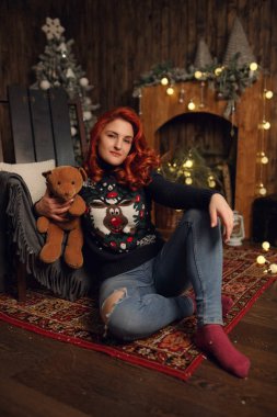 Çekici mutlu genç kadın rahat rahat giysiler içinde bir Noel ağacının yanında oturuyor