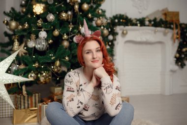 Çekici mutlu genç kadın rahat rahat giysiler içinde bir Noel ağacının yanında oturuyor