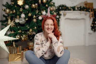 Çekici mutlu genç kadın rahat rahat giysiler içinde bir Noel ağacının yanında oturuyor
