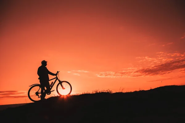 Sylwetka męskiej górskiej rowerzystę o zachodzie słońca w górach — Zdjęcie stockowe