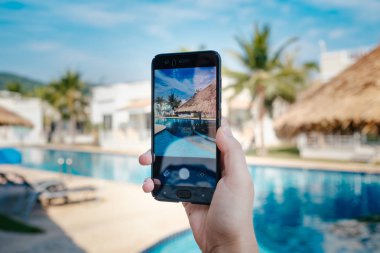 Otelde havuzun arka planda el tutarak telefon. ekranda fotoğraf kamerası.