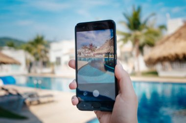 Otelde havuzun arka planda el tutarak telefon. ekranda fotoğraf kamerası.