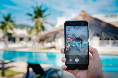 Otelde havuzun arka planda el tutarak telefon. ekranda fotoğraf kamerası.