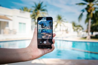 Otelde havuzun arka planda el tutarak telefon. ekranda fotoğraf kamerası.