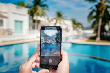 Otelde havuzun arka planda el tutarak telefon. ekranda fotoğraf kamerası.