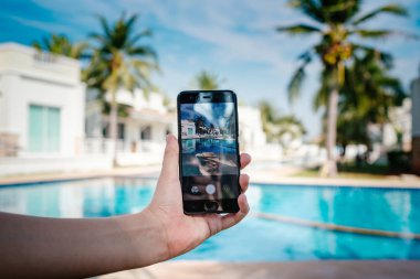 Otelde havuzun arka planda el tutarak telefon. ekranda fotoğraf kamerası.