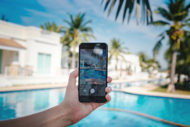 Otelde havuzun arka planda el tutarak telefon. ekranda fotoğraf kamerası.
