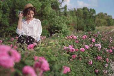 Güllerin yanında poz veren kıvırcık saçlı güzel bir kadın.