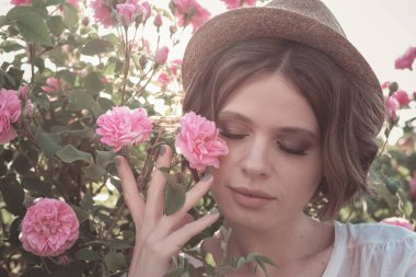 Güllerin yanında poz veren kıvırcık saçlı güzel bir kadın.