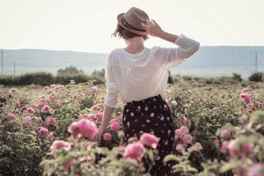 Güllerin yanında poz veren kıvırcık saçlı güzel bir kadın.
