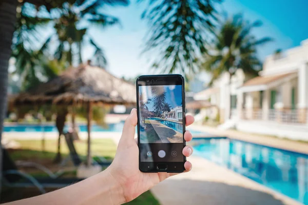 Otelde havuzun arka planda el tutarak telefon. ekranda fotoğraf kamerası.