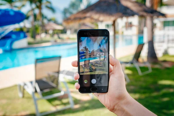 Otelde havuzun arka planda el tutarak telefon. ekranda fotoğraf kamerası.
