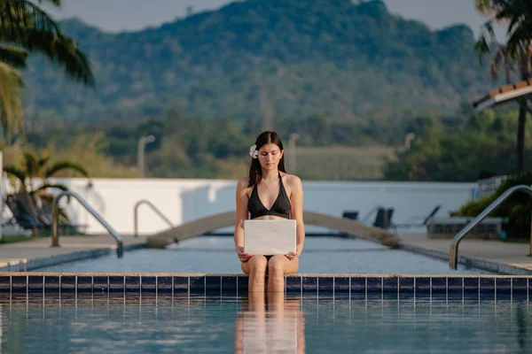 Güneşli bir günde havuz kenarında onu laptop kullanan kadın