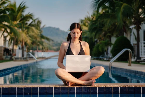 Женщина использует ноутбук на краю бассейна в солнечный день — стоковое фото