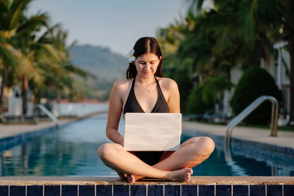 Жінка використовує свій ноутбук на краю басейну в сонячний день — стокове фото