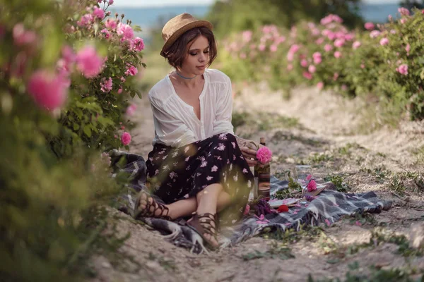 Hermosa chica usando sombrero con libro sentado en la hierba en rosa gaden — Foto de Stock