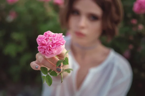 Belle jeune femme aux cheveux bouclés posant près des roses — Photo