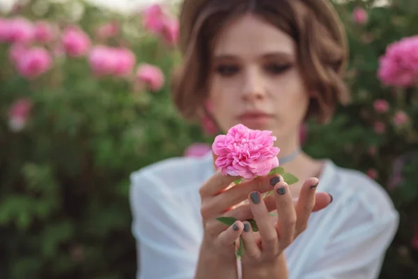 Belle jeune femme aux cheveux bouclés posant près des roses — Photo