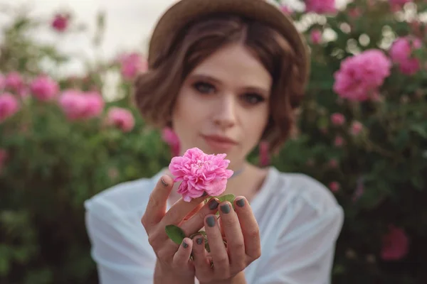 Bella giovane donna con i capelli ricci in posa vicino a rose — Foto Stock