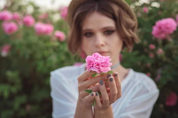 Bella giovane donna con i capelli ricci in posa vicino a rose — Foto Stock