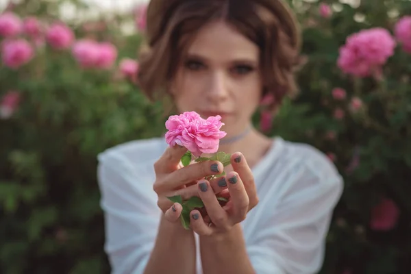 Bella giovane donna con i capelli ricci in posa vicino a rose — Foto Stock