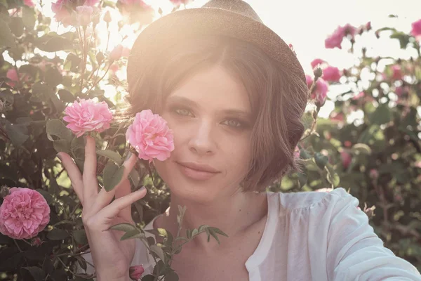 Güllerin yanında poz veren kıvırcık saçlı güzel bir kadın.