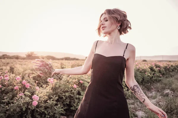 Güllerin yanında poz veren kıvırcık saçlı güzel bir kadın.