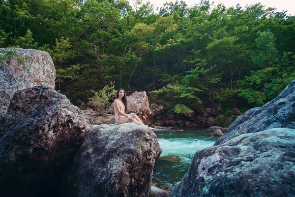 Elbise genç kadın bir dere ortasında taş oturuyor.