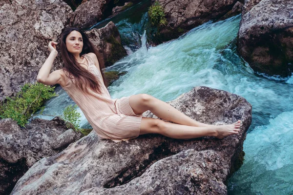 Giovane donna in abito è seduto sulla pietra nel mezzo di un torrente . — Foto Stock