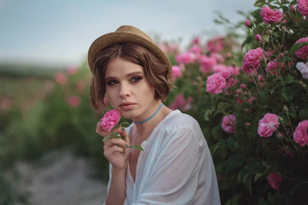 Hermosa joven con el pelo rizado posando cerca de rosas — Foto de Stock