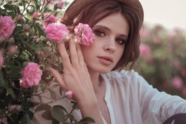 Güllerin yanında poz veren kıvırcık saçlı güzel bir kadın.