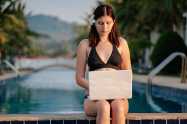 Güneşli bir günde havuz kenarında onu laptop kullanan kadın