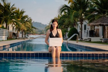 Güneşli bir günde havuz kenarında onu laptop kullanan kadın