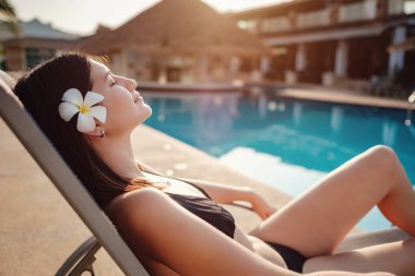 Lüks havuzun kenarında dinlenen genç bir kadının fotoğrafı. Yaz tatili.