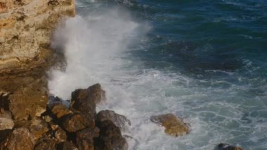 Deniz dalgaları kayalıklara çarpıyor ve bir gökkuşağı oluşturuyor, güzel bir günbatımı ışığı. yukarıdan görüntülendi.