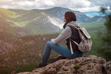Sırt çantasıyla gezen genç bir kadın ve rahatlatıcı bir ruh haliyle dağın tepesinde oturuyor ve ormanın, mavi gökyüzünün ve tatildeki bulutların güzel manzarasını seyrediyor. Asyalı kadın yalnız seyahat eder..