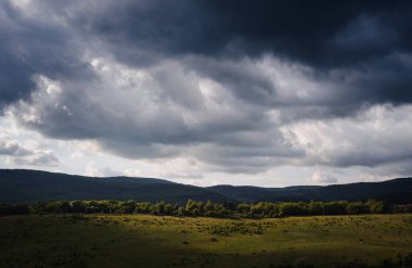 Koyu yağmur bulutları ve yeşil yamaçları aydınlatan güneş ışığı ile dramatik bir gökyüzü. Tepenin altında fantezi gökyüzü, her amaç için harika bir tasarım. Dağ yeşili vadi manzarası.
