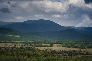 Fırtınadan önce dağların arasında resim gibi yeşil bir vadi. Kara bulutlar ve güneş ışınlarıyla dramatik bir gökyüzü. Arka planda bahar gökyüzü.