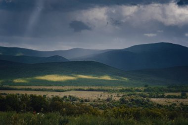 Fırtınadan önce dağların arasında resim gibi yeşil bir vadi. Kara bulutlar ve güneş ışınlarıyla dramatik bir gökyüzü. Arka planda bahar gökyüzü.