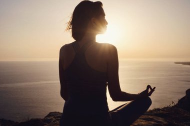 Gün batımı denizinde yoga yapan genç bir kadın. Nilüfer pozisyonunda meditasyon. Yoga silueti. Uyum ve meditasyon konsepti. Sağlıklı yaşam tarzı