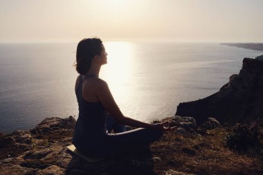 Gün batımı denizinde yoga yapan genç bir kadın. Nilüfer pozisyonunda meditasyon. Yoga silueti. Uyum ve meditasyon konsepti. Sağlıklı yaşam tarzı