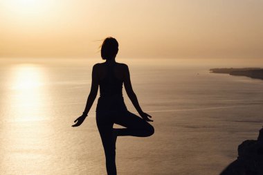 Gün batımında dağda yoga pozisyonu almış, dışarıda yoga yapan muhteşem genç bir kadının silueti. Sağlık, sağlık, spor ve yaşam tarzı kavramı