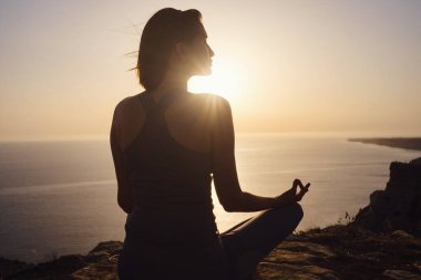 Gün batımı denizinde yoga yapan genç bir kadın. Nilüfer pozisyonunda meditasyon. Yoga silueti. Uyum ve meditasyon konsepti. Sağlıklı yaşam tarzı